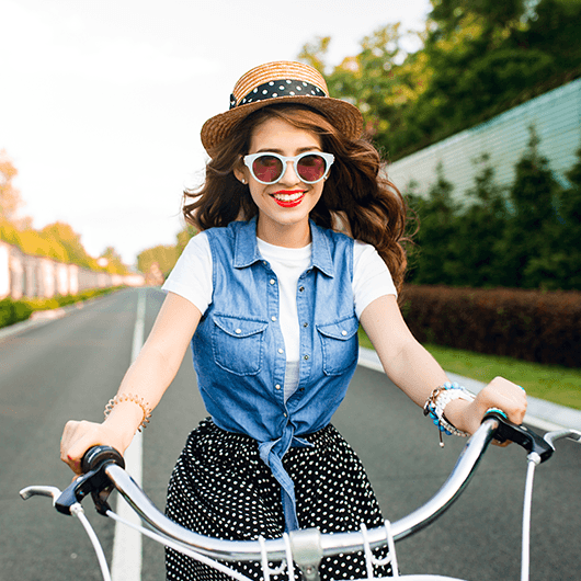 cute-girl-with-long-curly-hair-sunglasses-driving-bike-camera-road-she-wears-long-skirt-jerkin-hat-she-looks-happy_resized.png